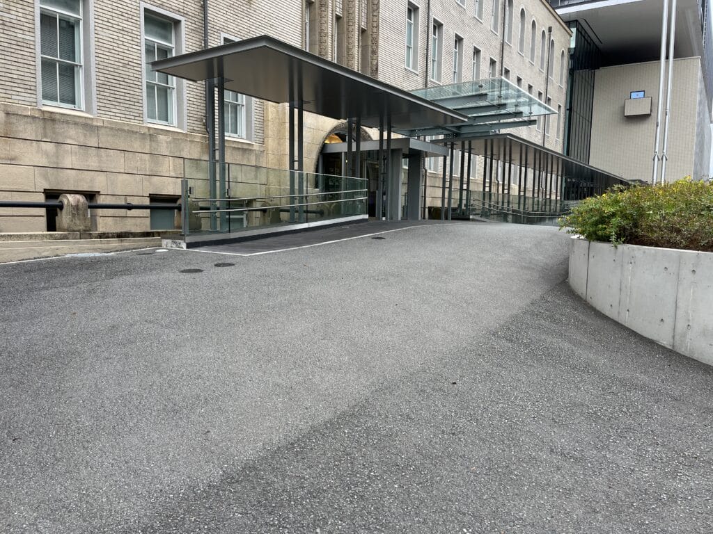 Exterior view of a modern brick building with a long glass-covered ramp and metal posts along the entrance area.