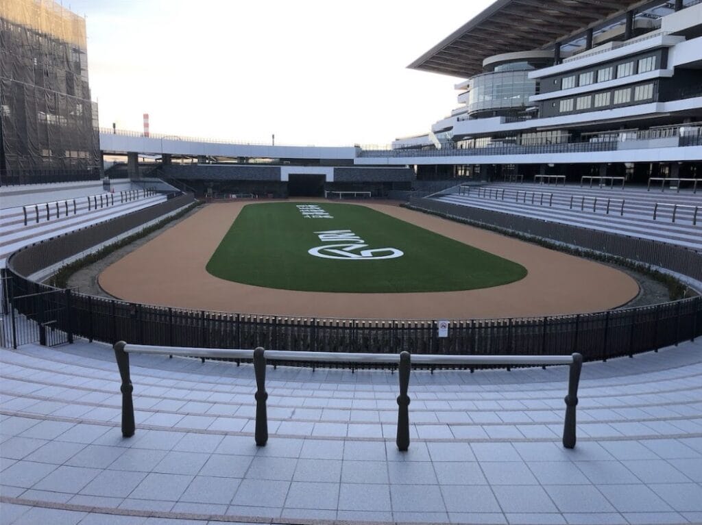 Empty modern stadium with an oval running track around a green infield featuring a large white logo; empty stands and glass-fronted facilities in the background.