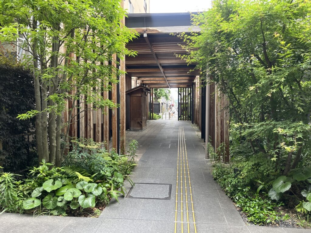 Covered wooden walkway flanked by lush greenery, with a tactile guiding path for pedestrians