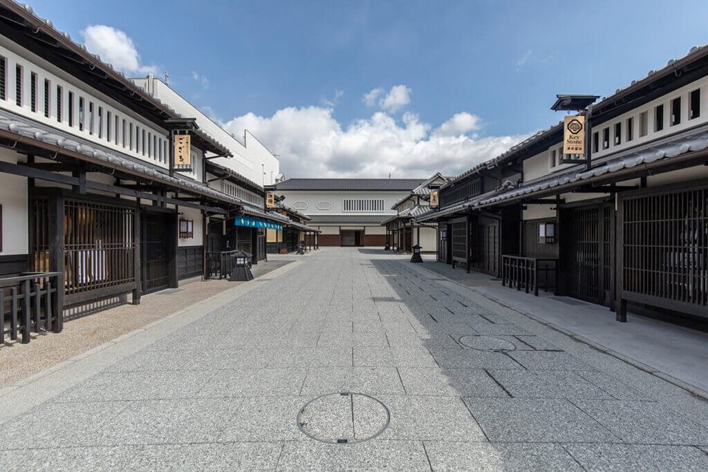 Empty traditional Japanese shopping street with white and dark wood storefronts, under a bright blue sky.
