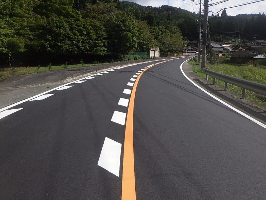 Curving rural road with an orange center line, white dashed lane markers, and a guardrail on the right.