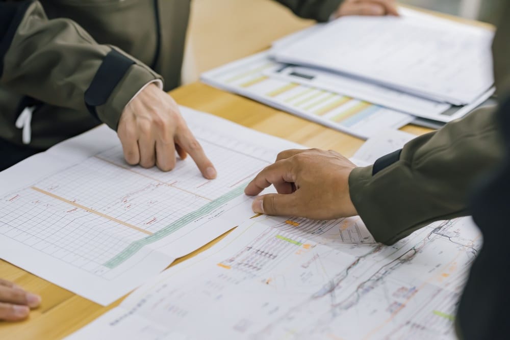 Two people study architectural blueprints on a wooden table, with one pointing at details.