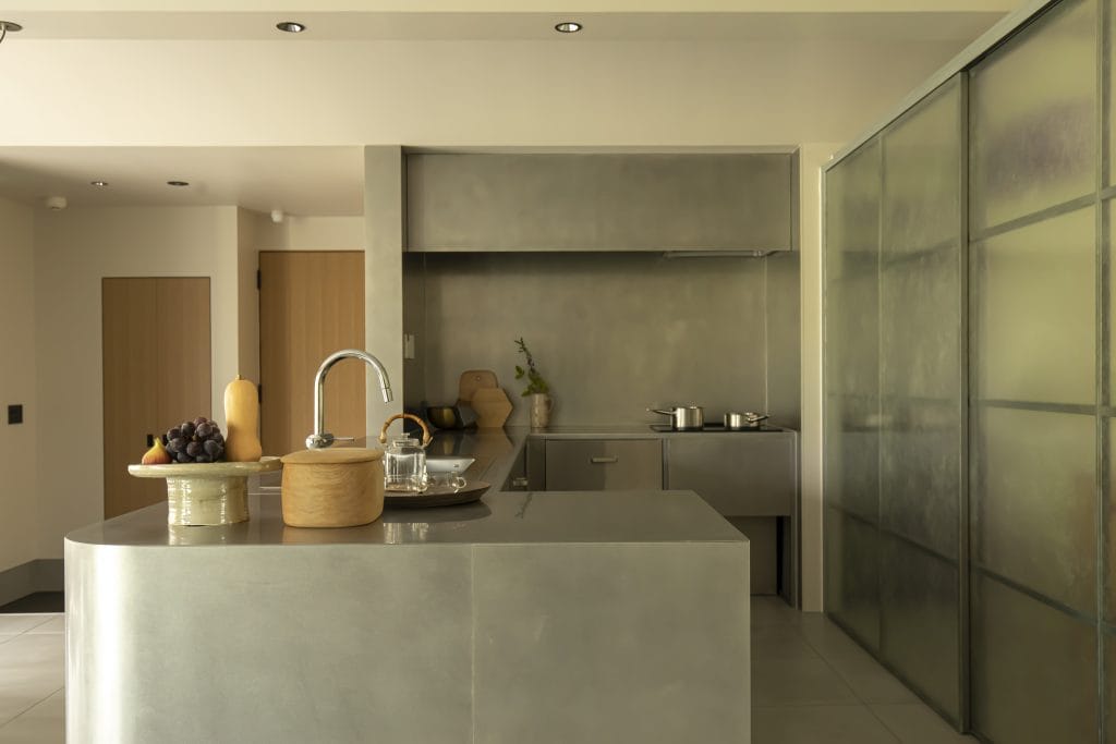 Modern stainless-steel kitchen with an island, sink, and glass wall on the right.