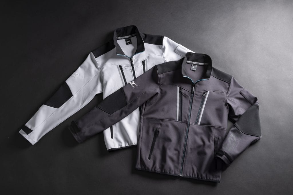 Two Mizuno color-block athletic jackets in light gray and dark gray with teal zipper accents laid on a dark surface.